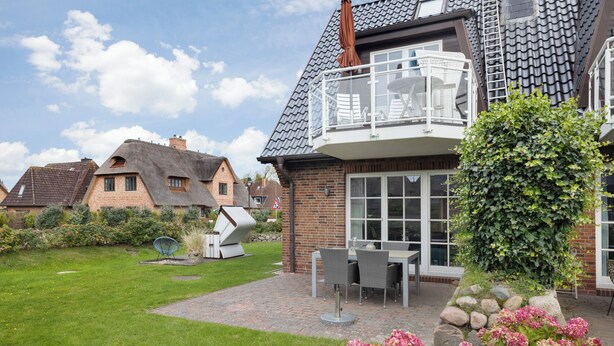 Een wooneiland met een bakstenen huis, een balkon met buitenmeubilair en een verzorgde tuin.