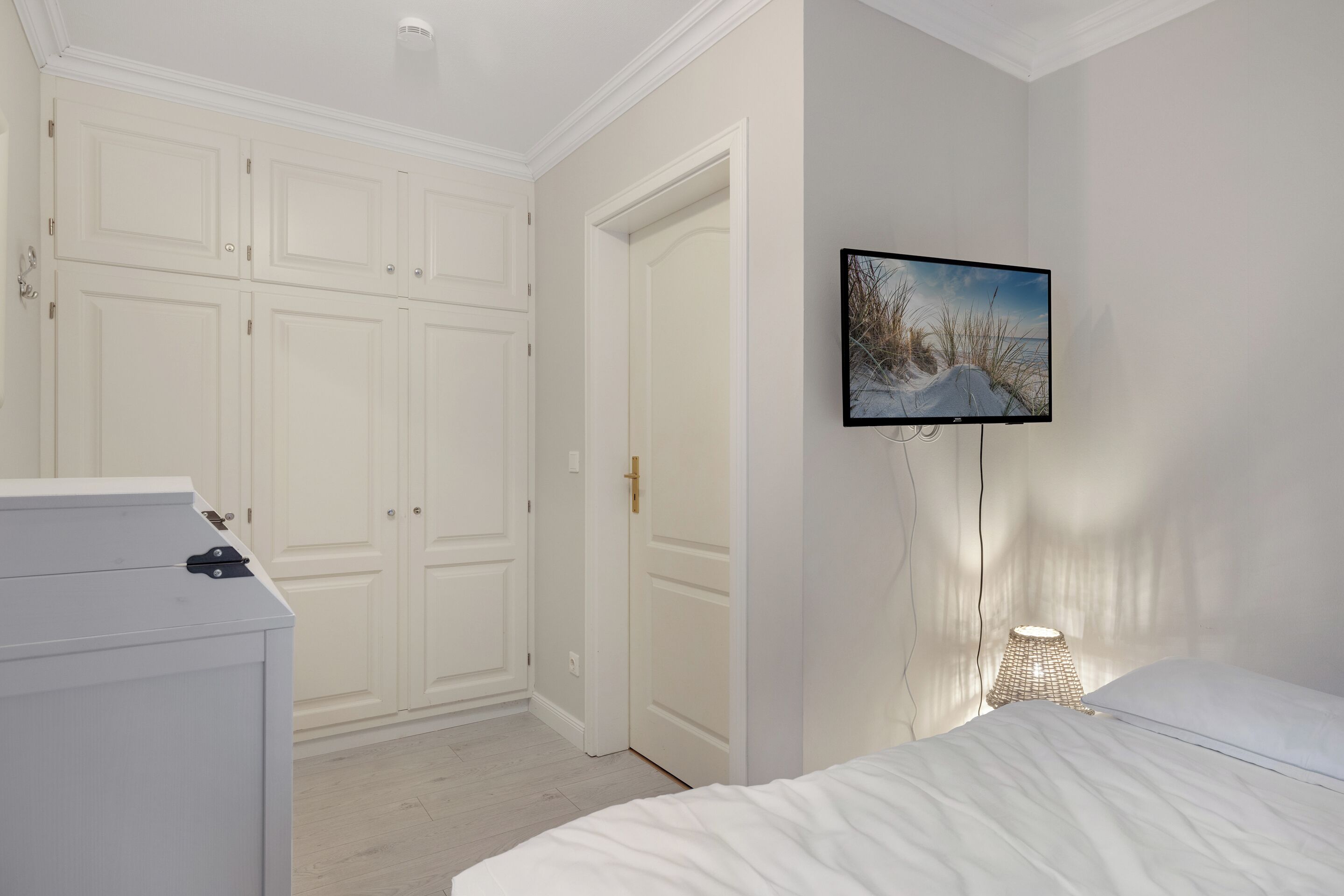 A bedroom with a bed, a dresser, a wardrobe, and a wall-mounted TV.