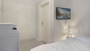 Een slaapkamer met een bed, een dressoir, een kledingkast en een tv aan de muur.