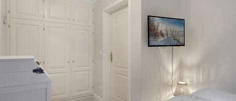 A bedroom with a bed, a dresser, a wardrobe, and a wall-mounted TV.