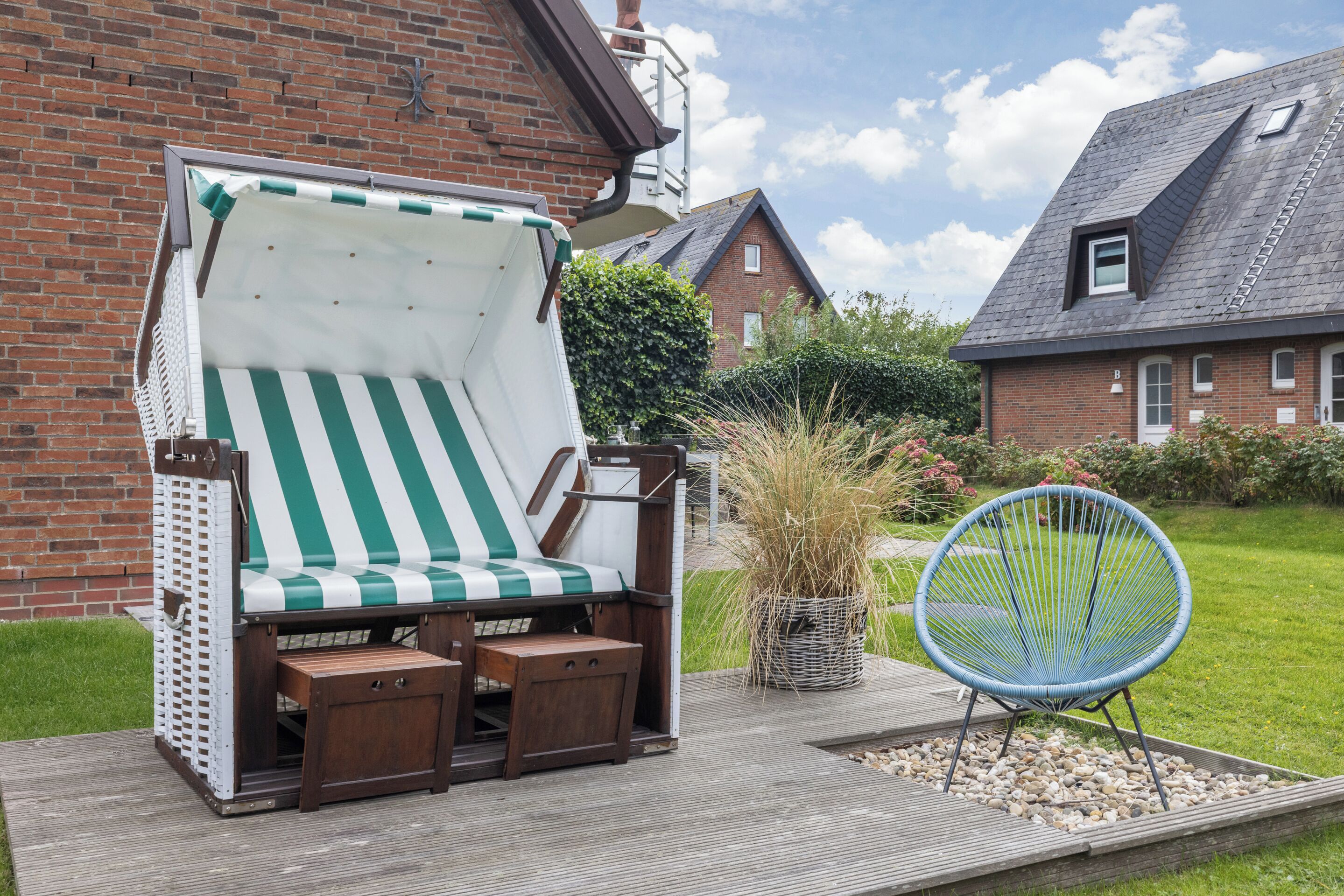 A wooden deck with a green and white striped lounge chair, a small wooden table, and a blue chair.
