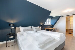 Relax in a spacious bedroom with a large bed, bedside tables, and a nightstand, featuring a sloped ceiling and a window.