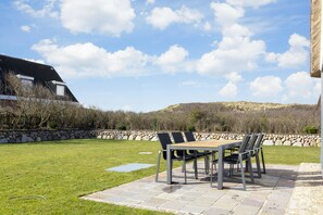 Relax on the patio surrounded by a lush lawn and a hillside view.