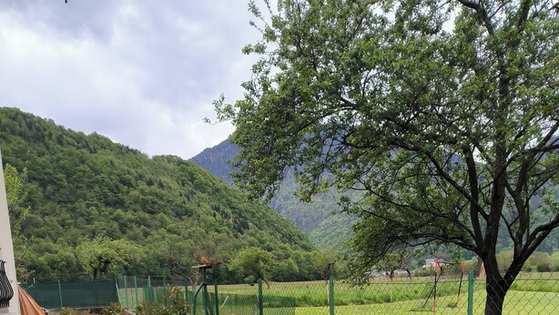 Un patio al aire libre con cubierta de madera, una mesa y sillas, y vistas a un paisaje verde con árboles y colinas.