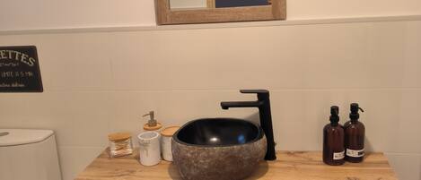 A bathroom with a wooden vanity, a round sink, and two bottles of soap.