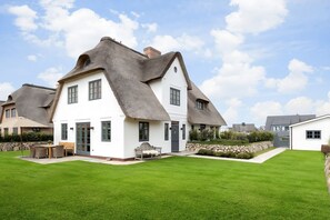Situated in a suburban setting, this house features a thatched roof and a well-maintained lawn with a patio.