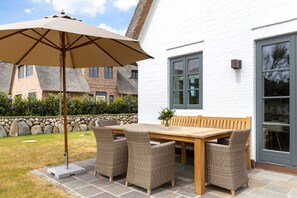 Relax on the patio with a comfortable table and chairs, shaded by a large umbrella.