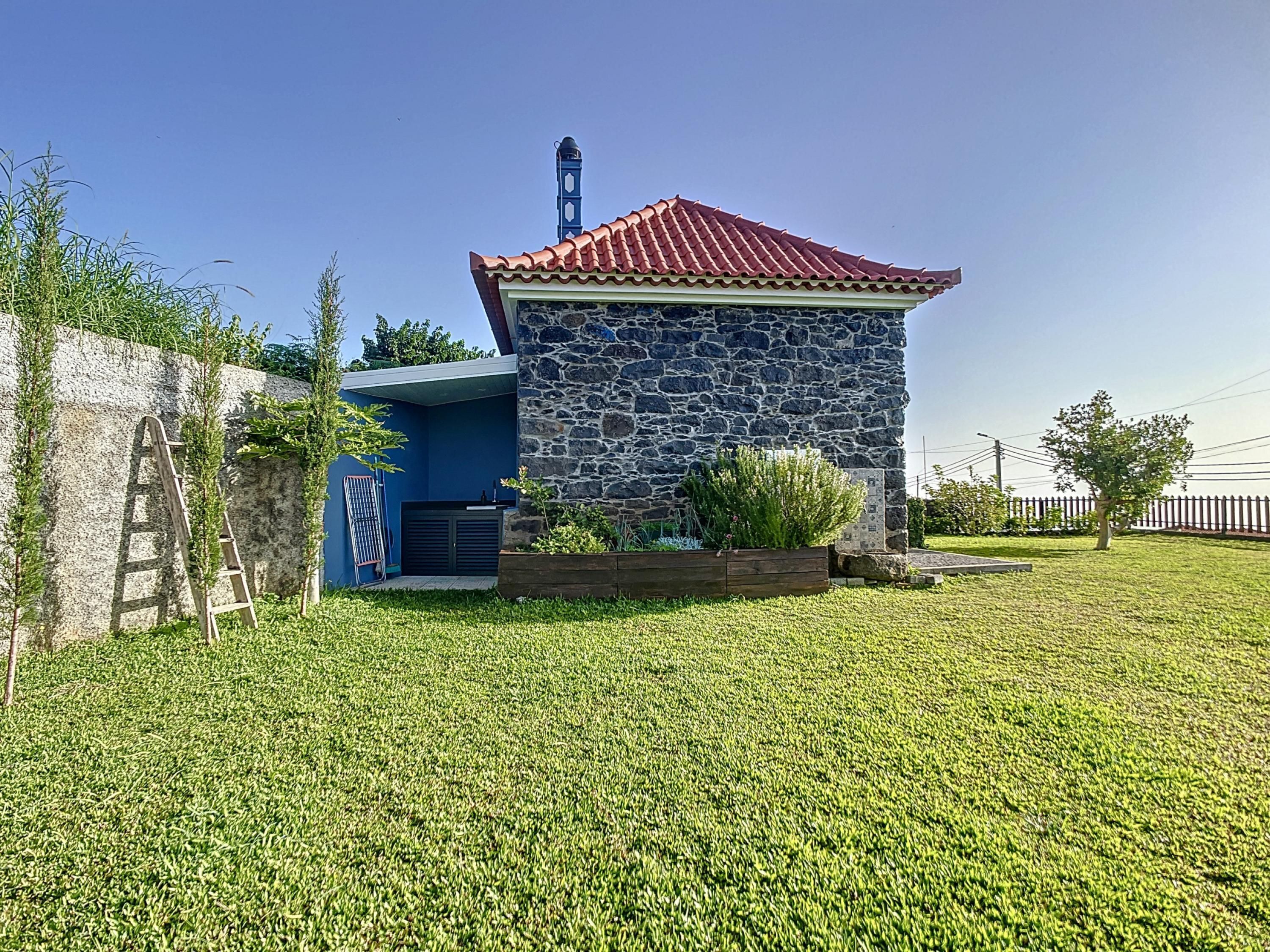 A stone building with a red roof, a blue exterior, and a small attached structure with a metal ladder.