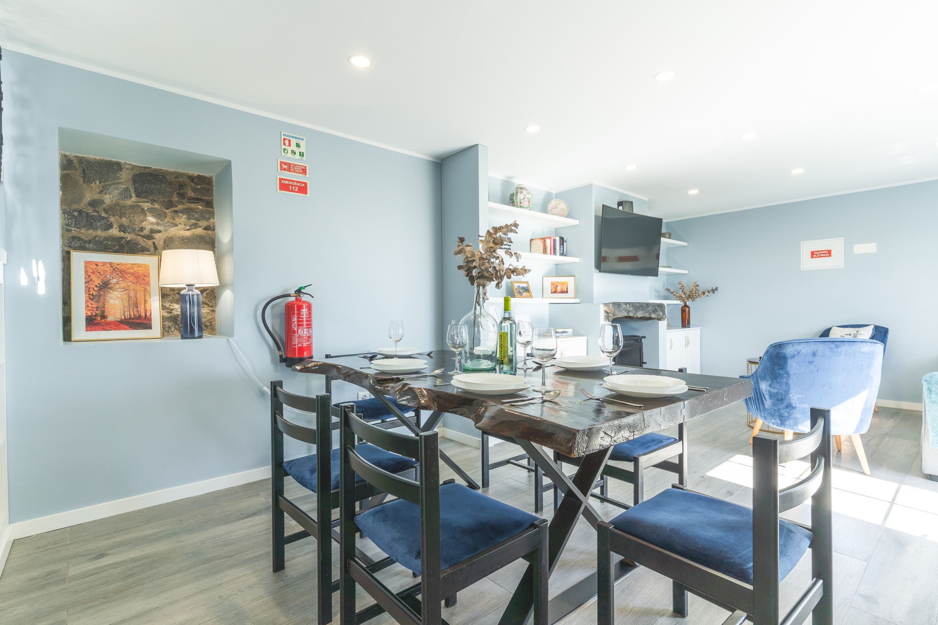A dining area with a wooden table, blue upholstered chairs, and a stone accent wall.