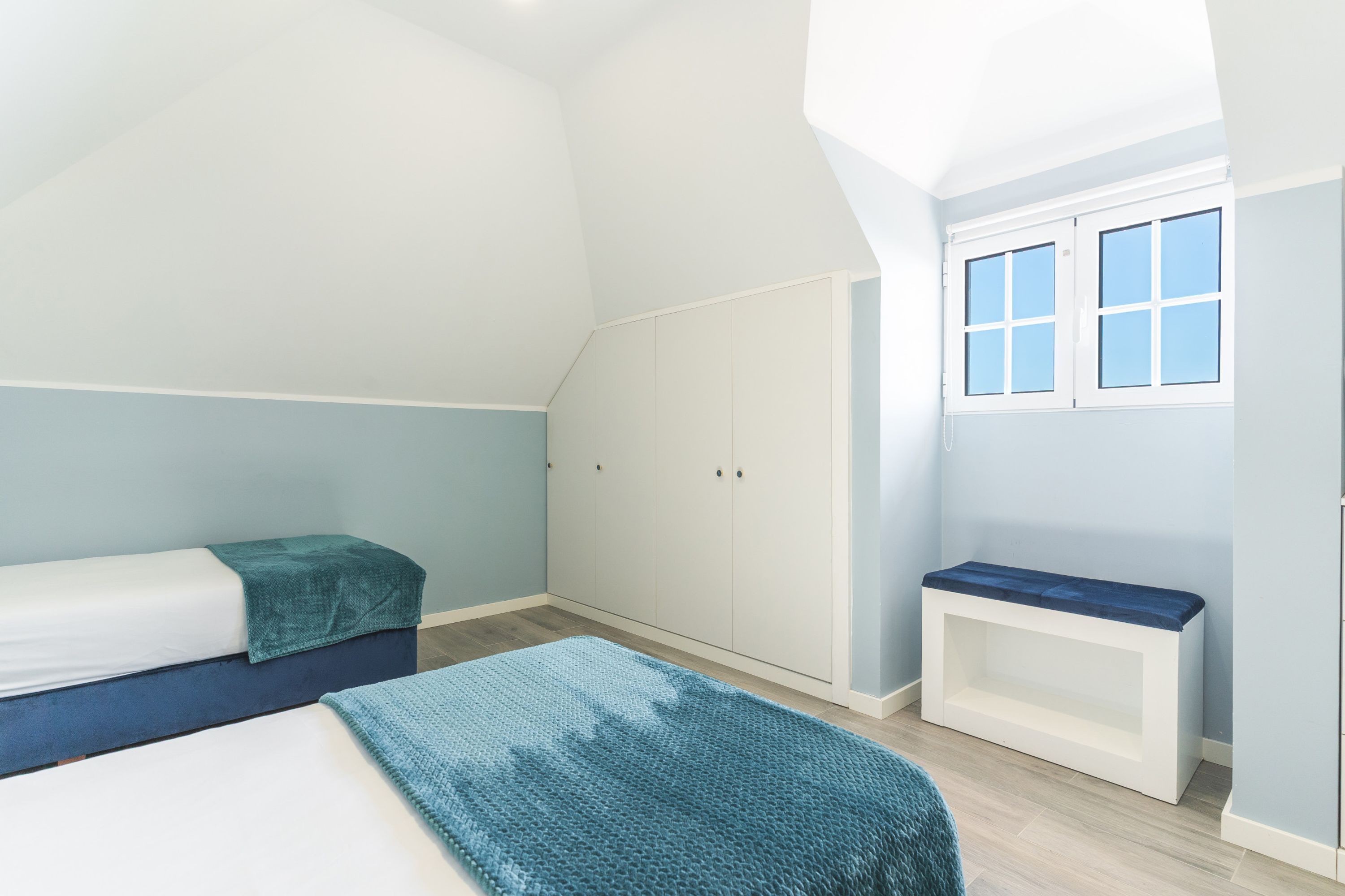 Une chambre avec un lit superposé, une armoire, un banc et une fenêtre.