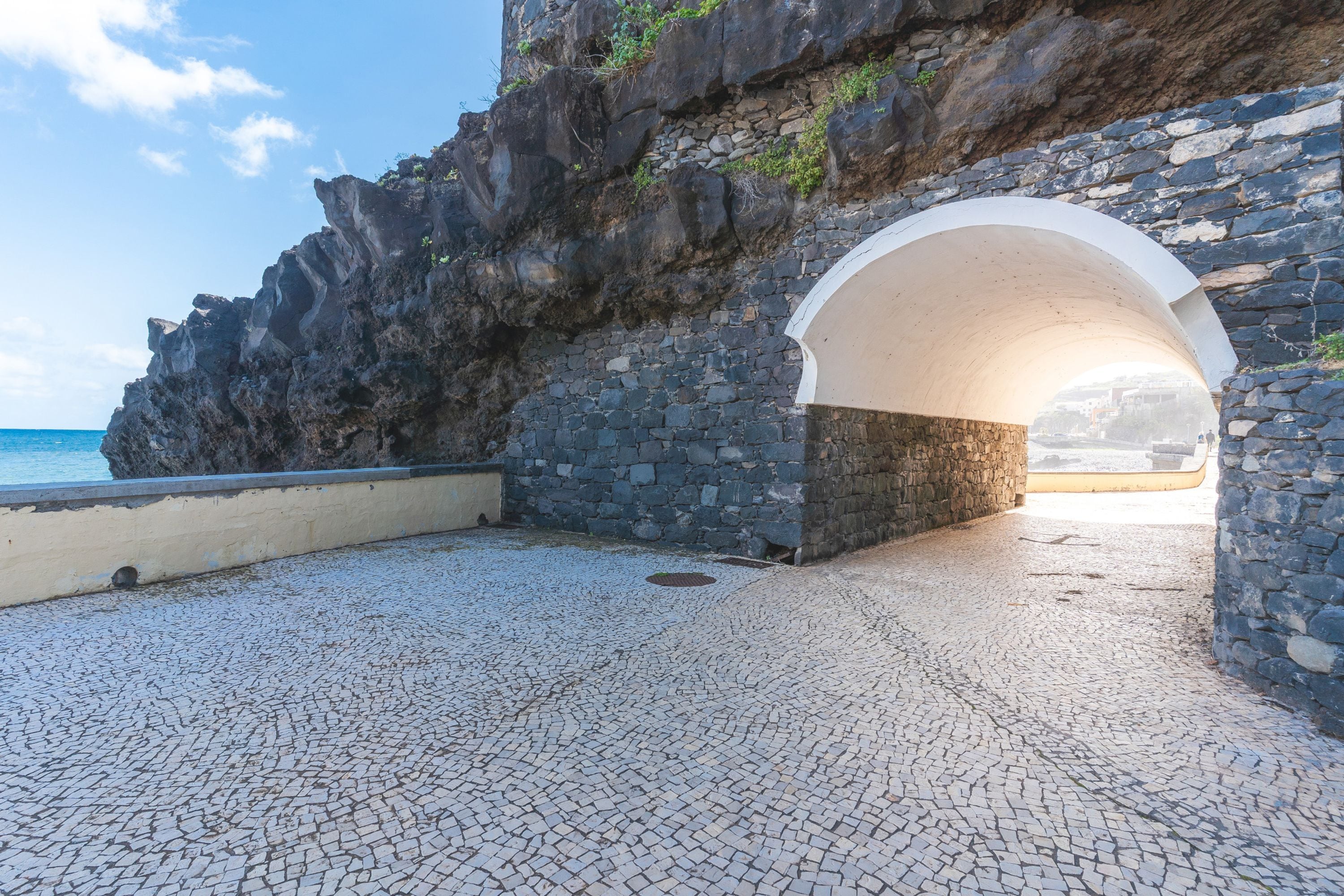 A stone archway leading to a cobblestone path by the sea.