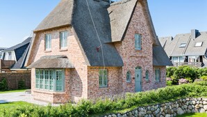 A traditional brick house with a steeply pitched thatched roof, multiple windows, and a stone wall in front. - In Bester, Strandnaher Lage Gelegenes, Freistehendes Luxus-haus Unter Reet (Wenningstedt-Braderup (Sylt))