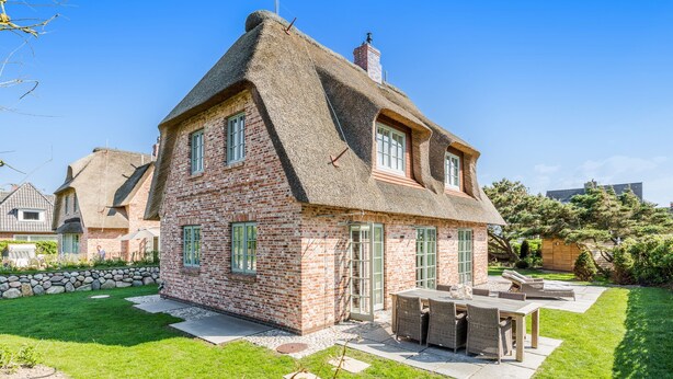A brick house with a thatched roof, a stone wall, and a patio with outdoor furniture. - In Bester, Strandnaher Lage Gelegenes, Freistehendes Luxus-haus Unter Reet (Wenningstedt-Braderup (Sylt))