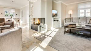 A modern living room with a fireplace, a sofa, a coffee table, and a dining area with a table and chairs. - In Bester, Strandnaher Lage Gelegenes, Freistehendes Luxus-haus Unter Reet (Wenningstedt-Braderup (Sylt))