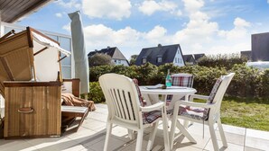 Un patio al aire libre con una mesa y sillas, un cofre de mimbre y vistas a casas en el fondo.