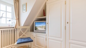 A room with a white radiator, a blue cushioned chair, a television on a shelf, and a white door.