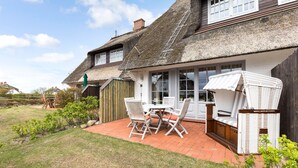 A thatched-roof house with a patio, a dining table with chairs, and a wicker sofa.