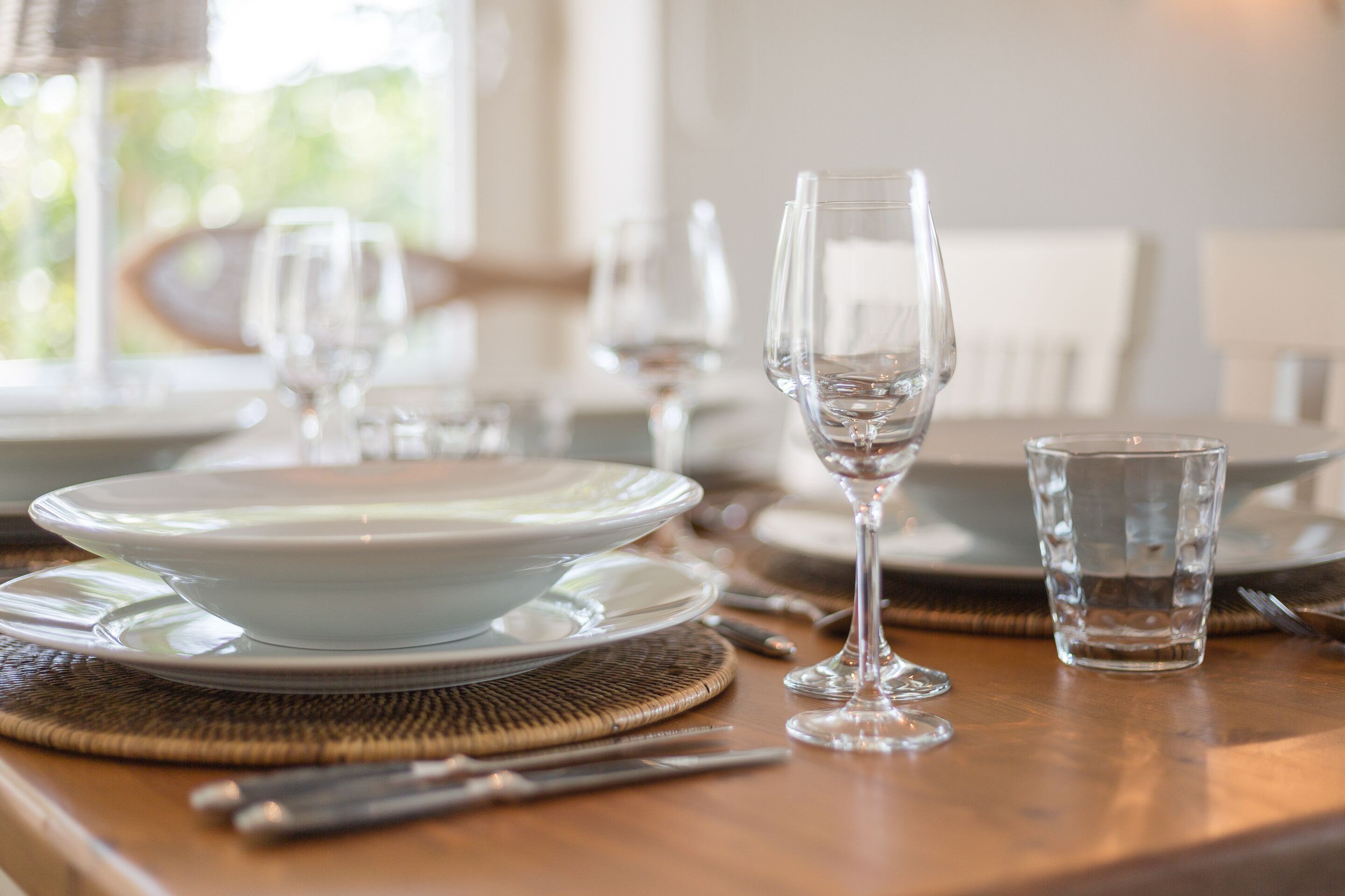 Une table à manger dressée avec de l’assiette blanche, des verres à vin transparents et un petit verre d’eau.