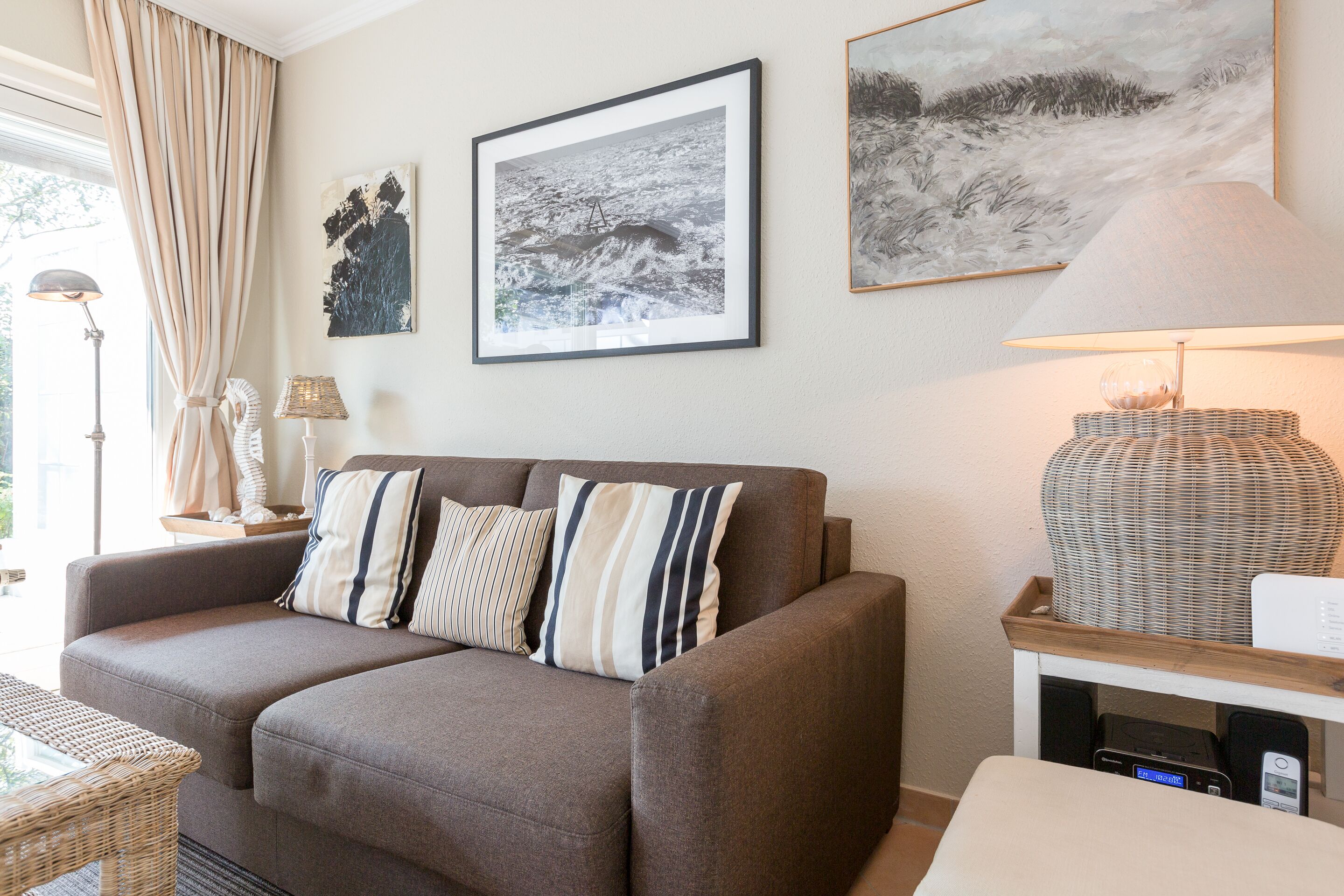 A living room with a brown sofa, striped pillows, a lamp, and two framed artworks on the wall.