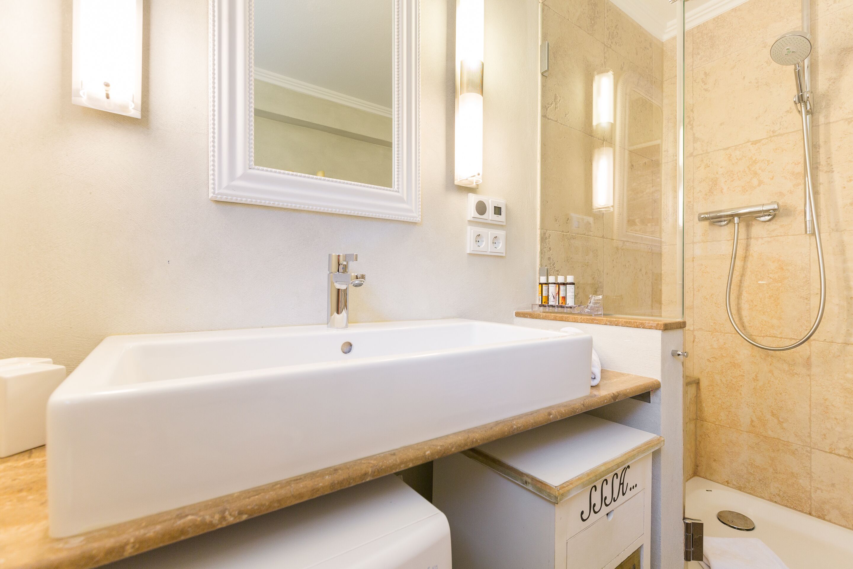 Un baño con un lavamanos blanco, un espejo, una ducha y un perchero para toallas.