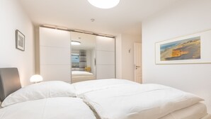 A bedroom with a bed, a wardrobe, a door, and a framed picture on the wall. - De-luxe village pond flair. (Wenningstedt-Braderup (Sylt))