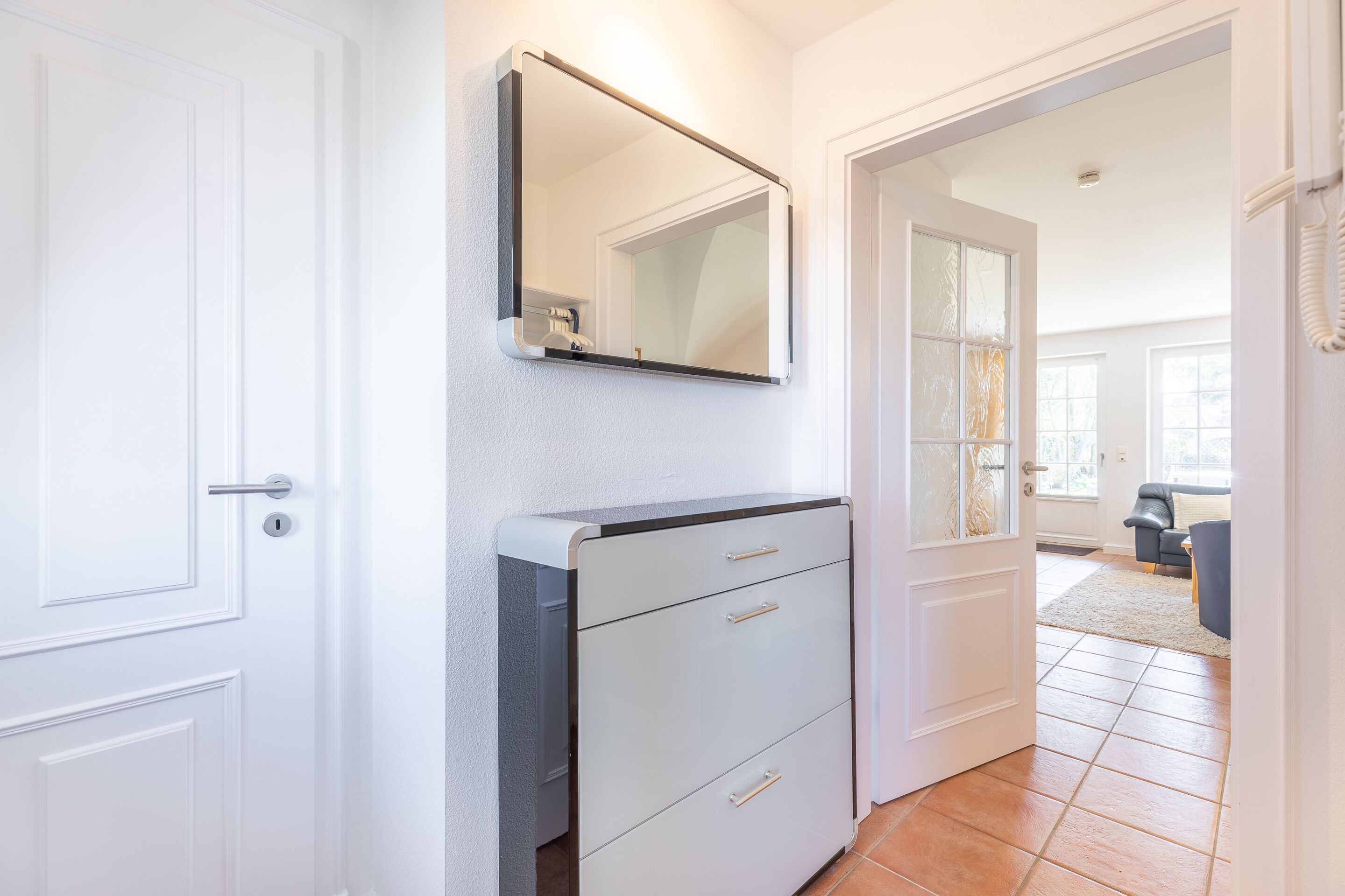 Un couloir avec une porte blanche, un classeur gris et un miroir accroché au mur.