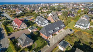 Vue aérienne d’un quartier résidentiel avec des maisons, un parking et une vue sur la mer.