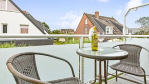 Un balcon avec des fauteuils en osier et une table en verre, donnant sur un quartier résidentiel avec des maisons.