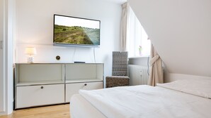 Une chambre à coucher avec un lit, un téléviseur fixé au mur, une table de chevet, une lampe et une fenêtre avec des rideaux.