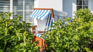 A white brick building with large windows and a blue and white striped awning over a wooden chair. - Completely ground floor 3-room apartment near the beach. (Wenningstedt-Braderup (Sylt))