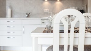 A modern kitchen with white cabinetry, a dining table set with glasses and cutlery, and a neutral backsplash. - Completely ground floor 3-room apartment near the beach. (Wenningstedt-Braderup (Sylt))