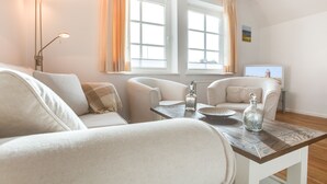 Una sala de estar moderna con un sofá, dos sillones, una mesita de centro y un televisor.