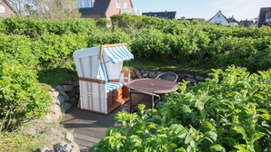 Un jardín con una terraza de madera, una silla de mimbre y un toldo a rayas, junto a una mesa redonda.