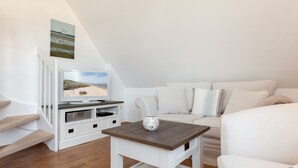 A modern living room with a flat-screen TV, a white sofa, a small wooden coffee table, and a staircase leading to an upper level. - 2-raum-appartement im OG und DG, ca. 43qm² Nutzfläche für bis zu 2 Personen (Wenningstedt-Braderup (Sylt))