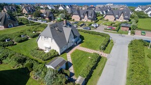 An aerial view of a residential area with houses, a well-maintained lawn, and a clear view of the sea. - 2-raum-appartement im OG und DG, ca. 43qm² Nutzfläche für bis zu 2 Personen (Wenningstedt-Braderup (Sylt))