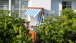A white building with a window, a blue and white striped awning, and a wooden chair with a striped cushion. - Willkommen in der Heideresidenz auf Sylt! (Wenningstedt-Braderup (Sylt))