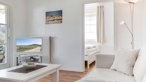 A modern living room with a television, a dining table, a sofa, and a painting on the wall. - Willkommen in der Heideresidenz auf Sylt! (Wenningstedt-Braderup (Sylt))