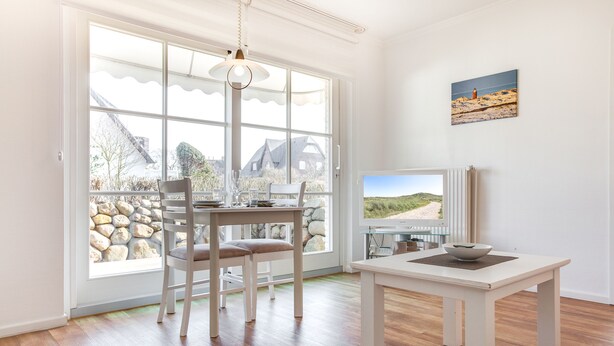 A bright room with a large window, a table with chairs, and a painting on the wall. - Willkommen in der Heideresidenz auf Sylt! (Wenningstedt-Braderup (Sylt))