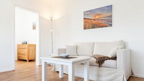 A minimalist living room with a white sofa, a white coffee table, and a wooden cabinet. - Willkommen in der Heideresidenz auf Sylt! (Wenningstedt-Braderup (Sylt))