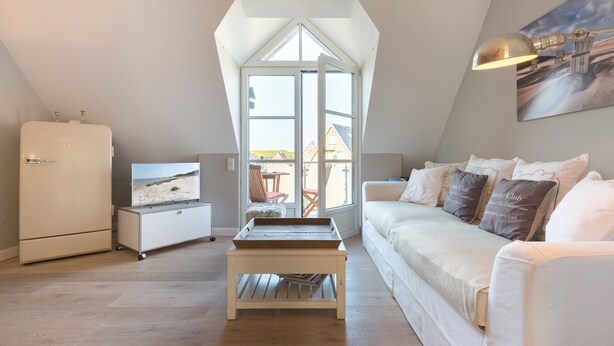 A modern loft bedroom with a sloped ceiling, a white sofa, a small table, and a refrigerator. - Fantastisch Strandnahe Lage & Beach-style Wohlfühl-atmosphäre (Sylt / OT Westerland)
