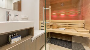 Ein modernes Badezimmer mit einer Duschkabine aus Glas, Holzsitzen und einem Waschtisch mit Pflegeprodukten.