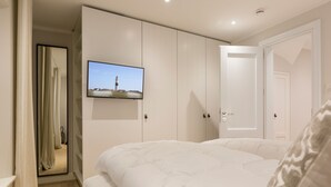 Ein Schlafzimmer mit einem großen Bett, einem Kleiderschrank, einem an der Wand montierten Fernseher und einer Tür zu einem anderen Raum.