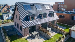 Ein modernes Haus mit einem geneigten Dach, Solaranlagen und einer Steinterrasse mit Gartenmöbeln.