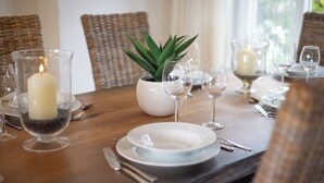 A dining table set with plates, cutlery, and wine glasses, with a candle and a potted plant in the center.