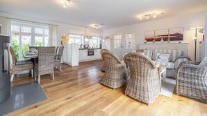A spacious living area with wicker furniture, a kitchen in the background, and a dining area with a table and chairs.