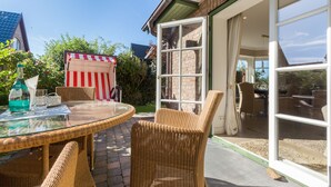 Ein Tisch mit Glasplatte, Korbstühle, ein gestreiftes Tuch und Blick auf den Garten durch eine Glastür.