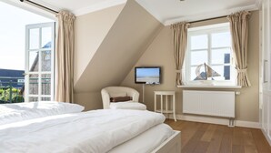Ein Schlafzimmer mit zwei Betten, einem Fernseher, einem kleinen Tisch und einem Fenster mit Vorhängen.