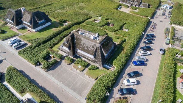 An aerial view of a property with a large parking lot, several buildings with thatched roofs, and a beach in the background. - The most beautiful views! (Wenningstedt-Braderup (Sylt))