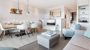 Una sala de estar moderna con comedor, sofá, mesa de centro y televisor.