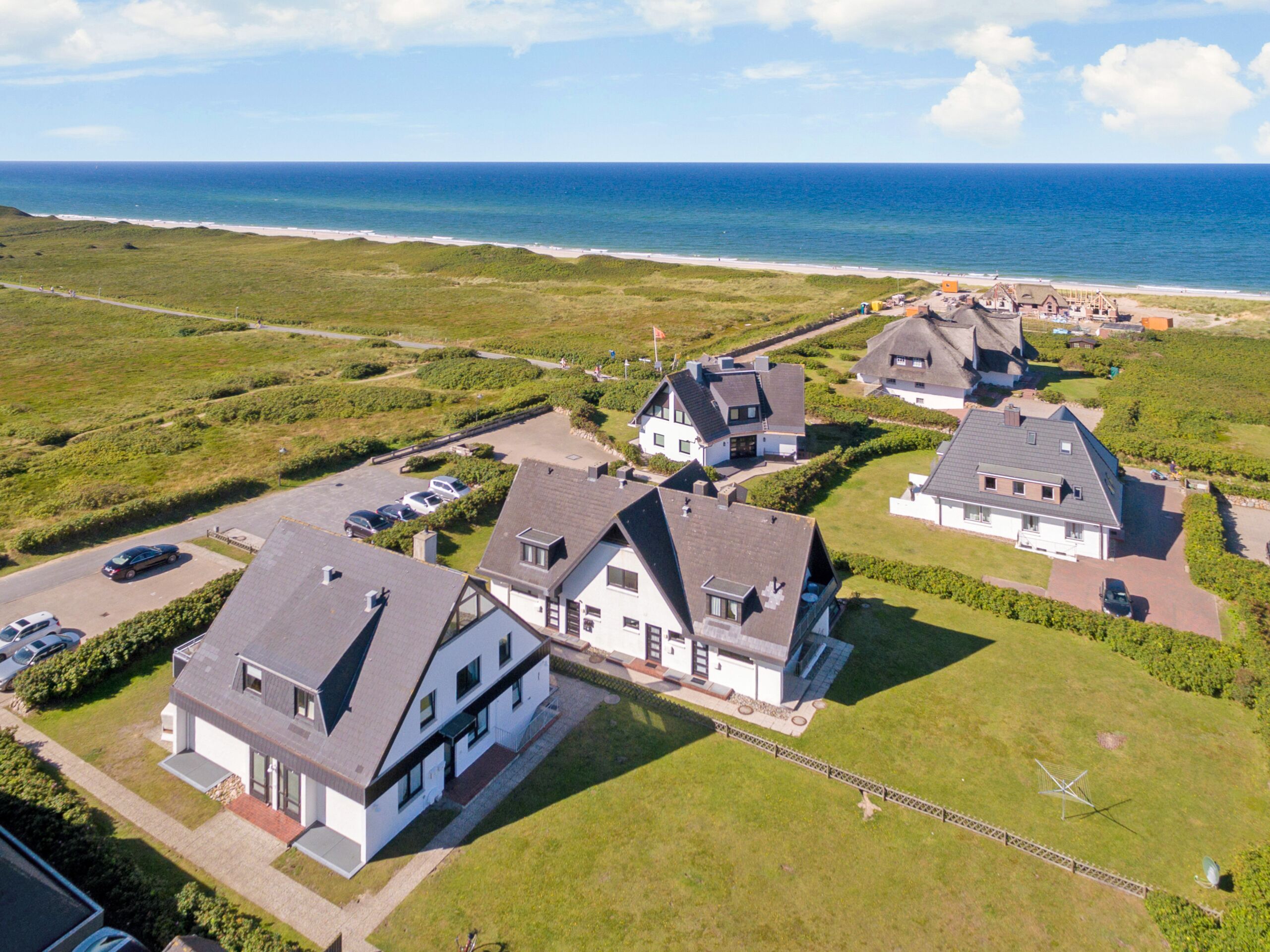 Una zona residenziale costiera con case dai tetti ripidi e facciate bianche, immersa in campi verdi e affacciata su una spiaggia.